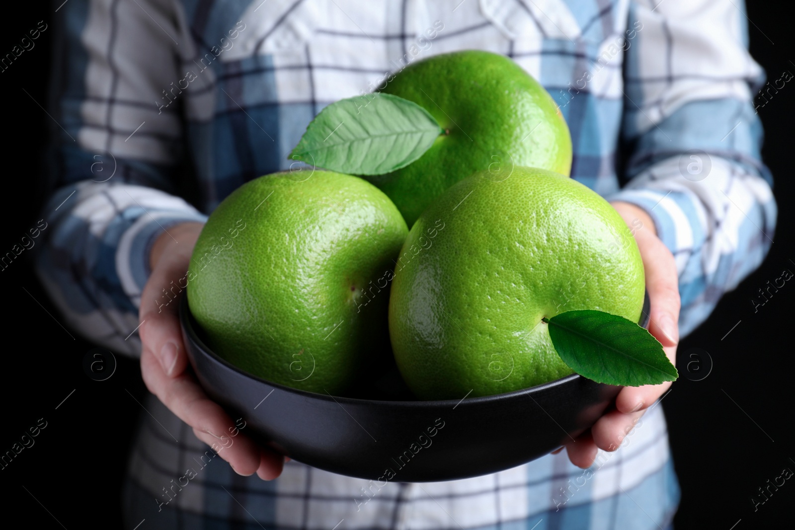 Photo of Woman holding bowl with sweetie fruits on black background, closeup