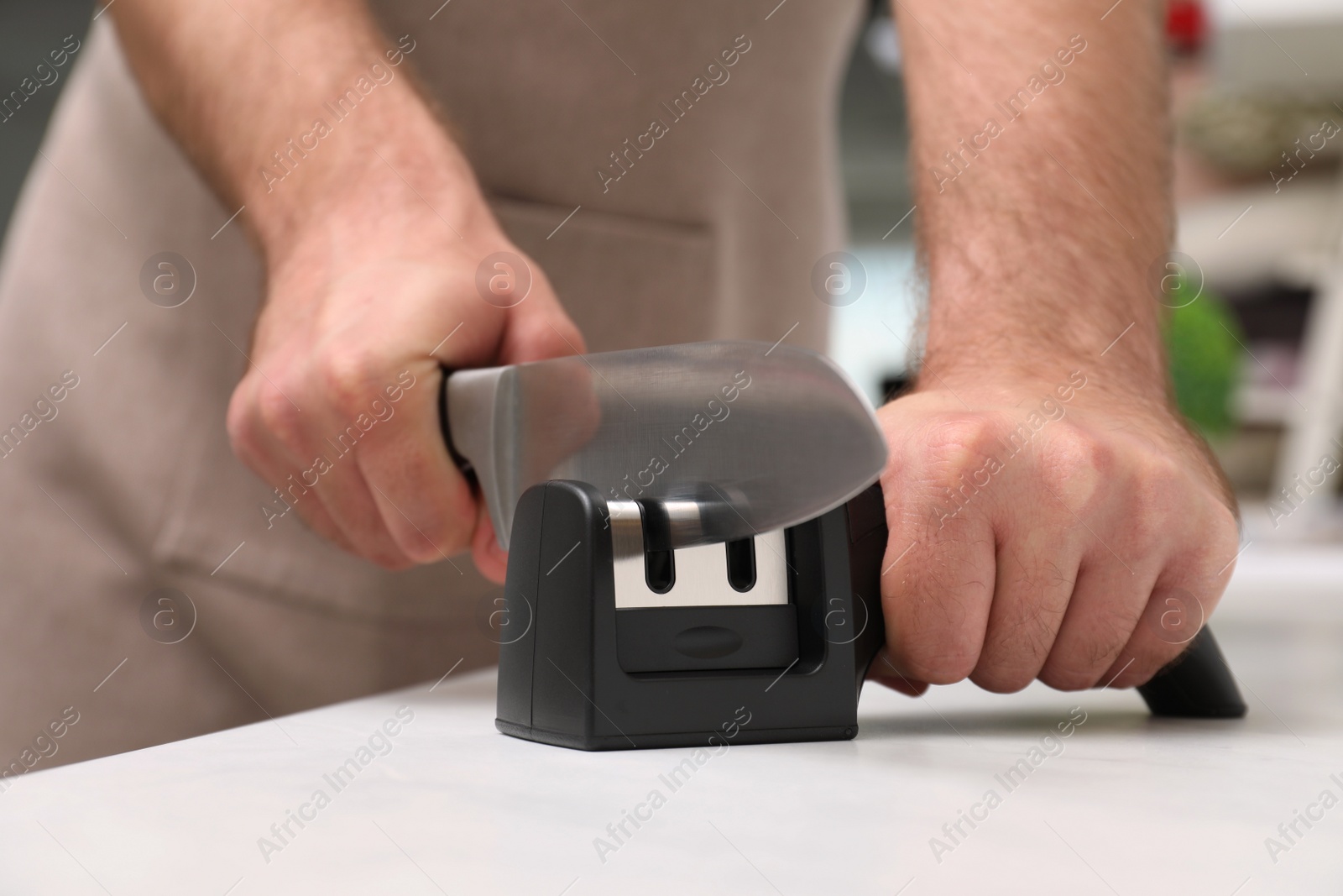 Photo of Man sharpening knife at white table indoors, closeup