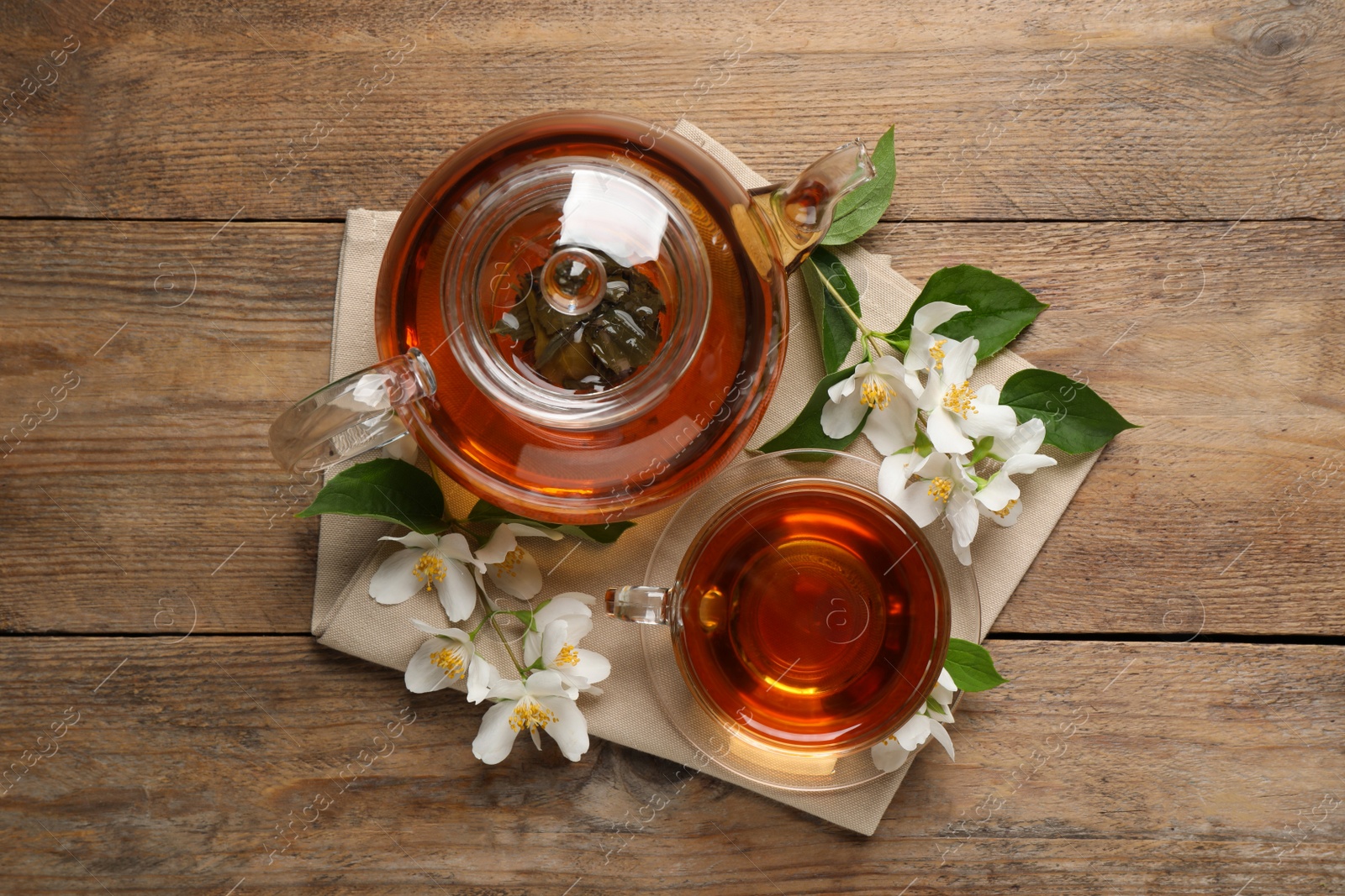 Photo of Aromatic jasmine tea and fresh flowers on wooden table, flat lay