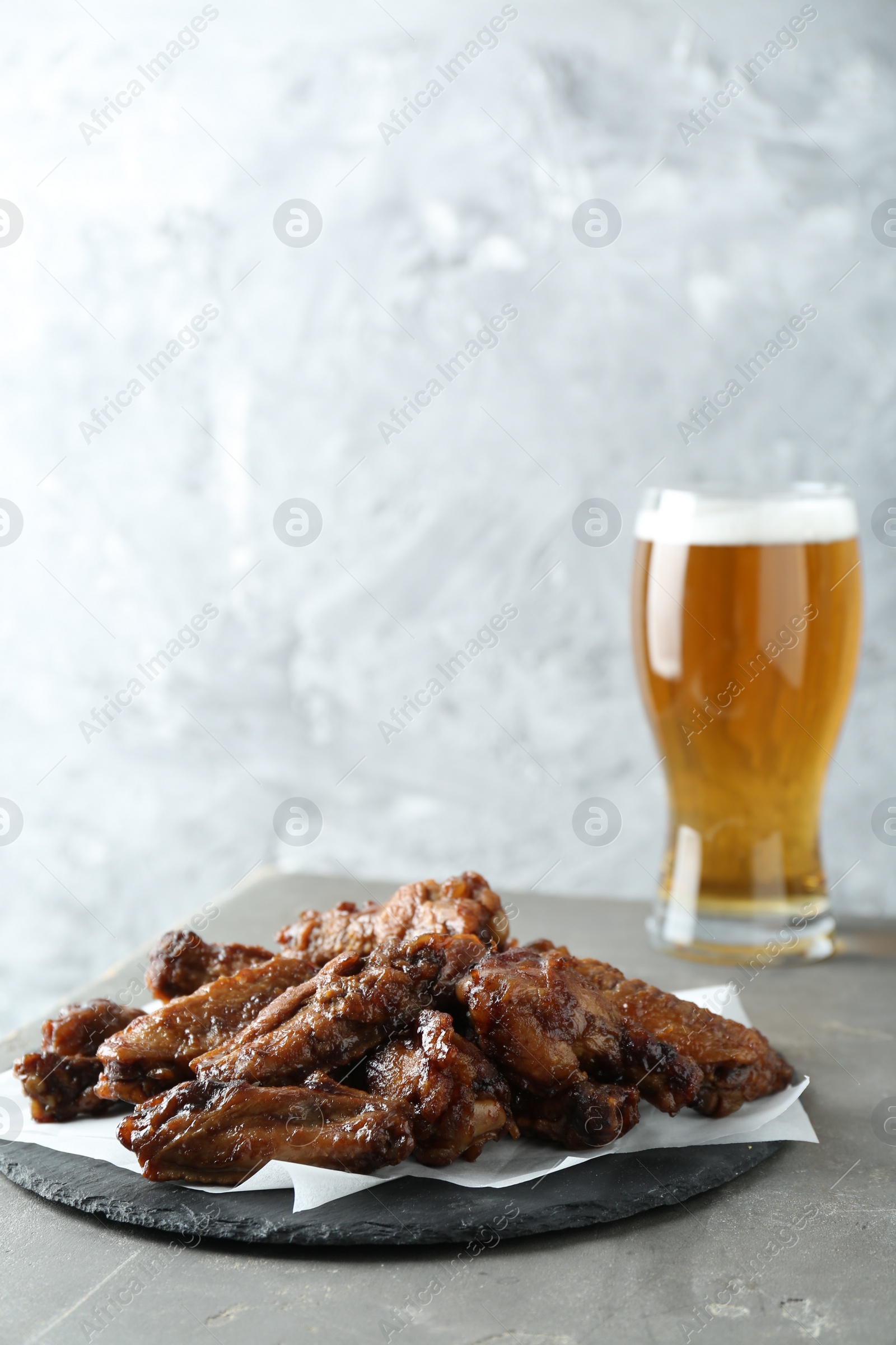 Photo of Delicious chicken wings and glass of beer on grey table. Space for text