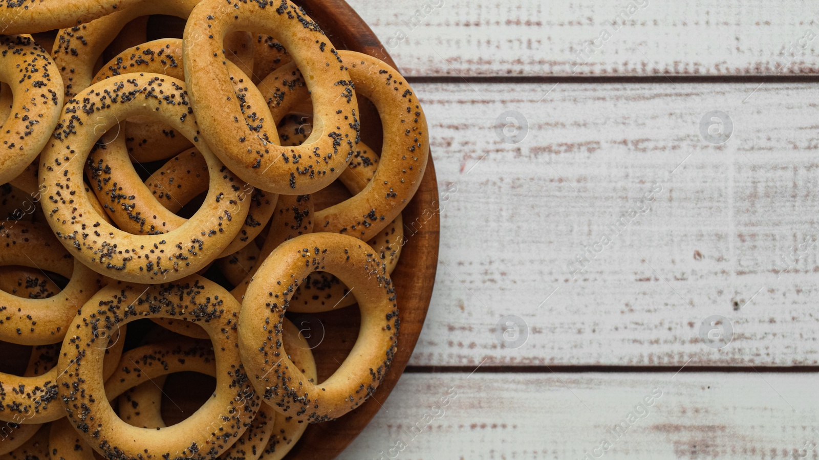 Photo of Plate with delicious ring shaped Sushki (dry bagels) on white wooden table, top view. Space for text