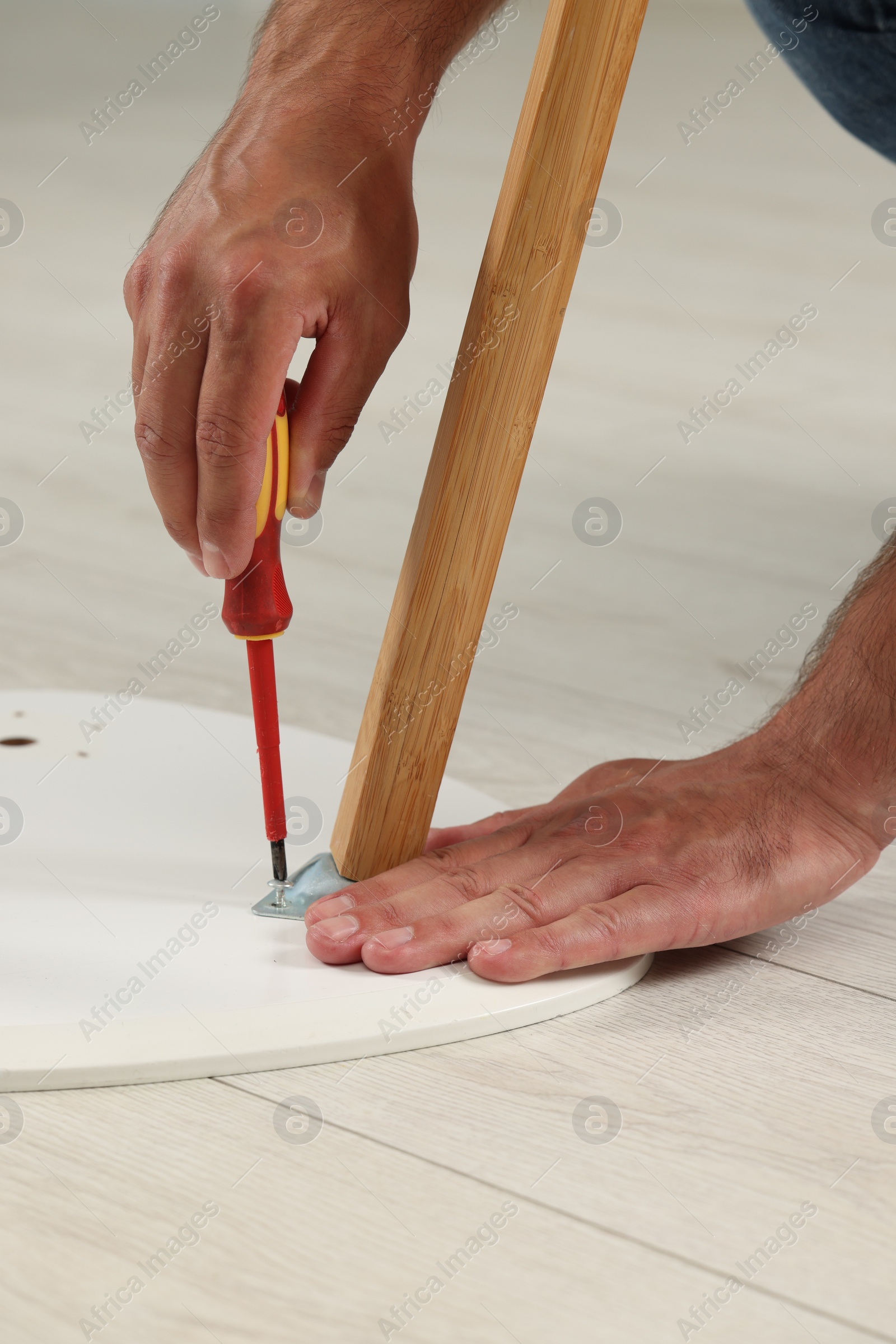Photo of Man with screwdriver assembling furniture on floor indoors, closeup