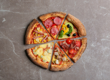 Photo of Slices of different delicious pizzas on grey marble table, flat lay