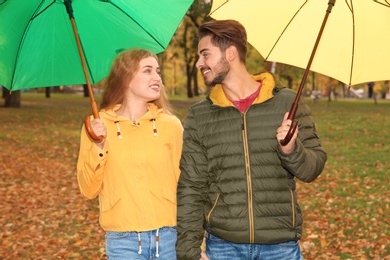 Happy couple with umbrellas walking in park