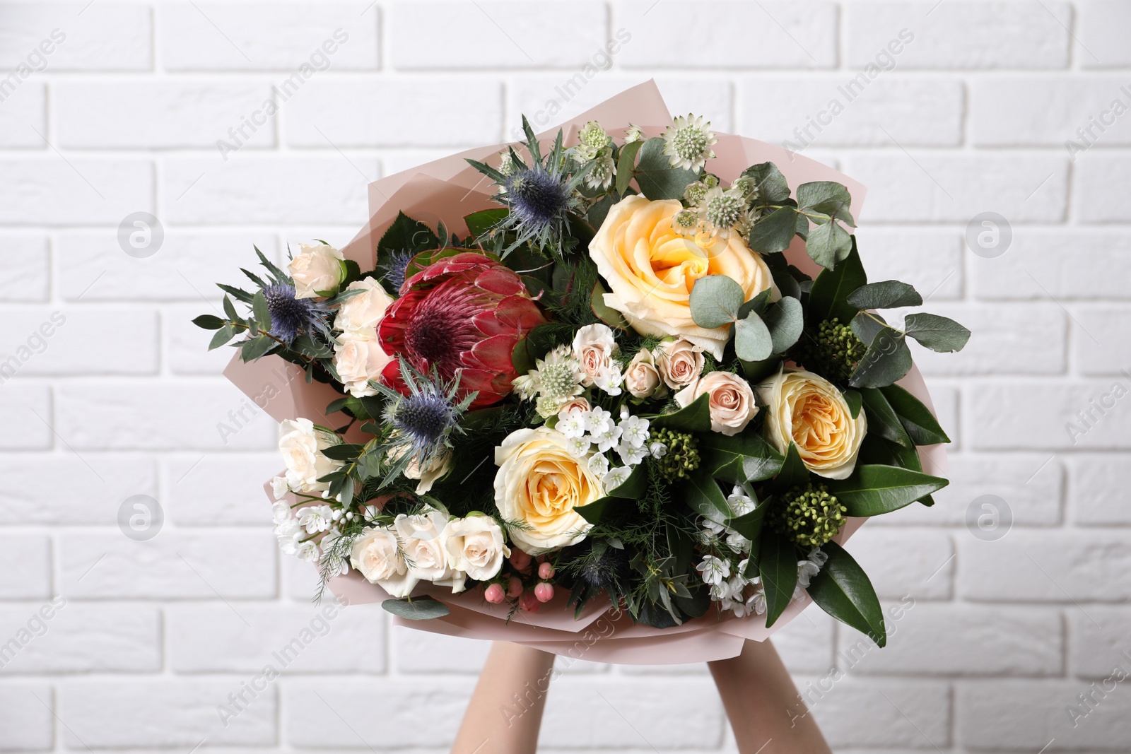 Photo of Woman with bouquet of beautiful roses near white brick wall, closeup