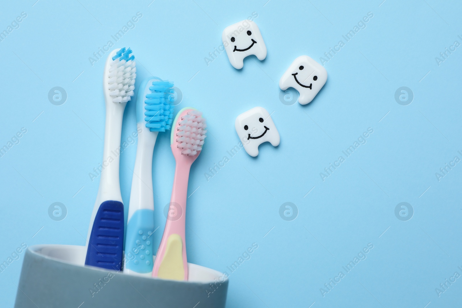 Photo of Plastic teeth with cute faces and toothbrushes on light blue background, flat lay. Space for text