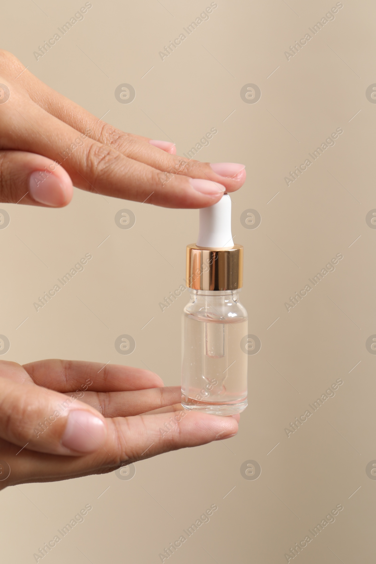 Photo of Woman with bottle of cosmetic serum on beige background, closeup