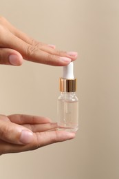 Photo of Woman with bottle of cosmetic serum on beige background, closeup