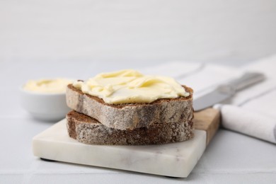 Photo of Slices of tasty bread with butter on white tiled table, closeup. Space for text