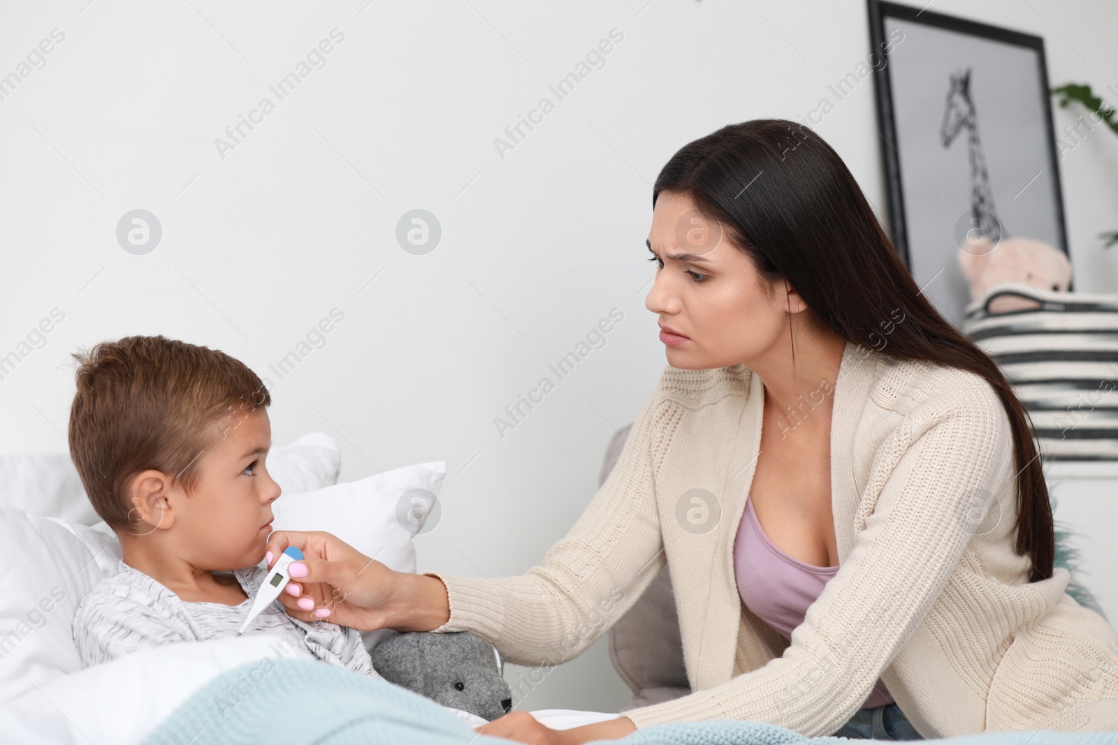 Photo of Mother measuring temperature of her sick son in bed