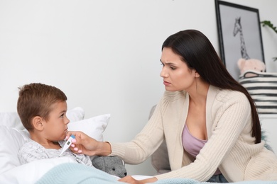 Mother measuring temperature of her sick son in bed