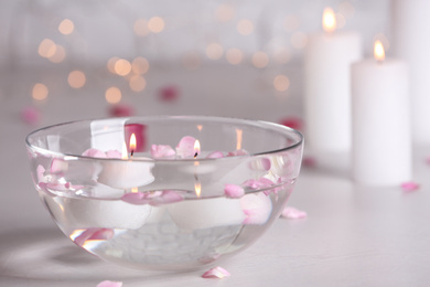 Photo of Glass bowl with burning candles and petals on grey stone table