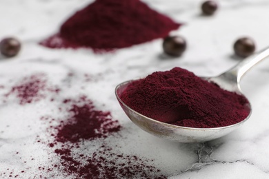 Photo of Spoon with acai powder on marble table, closeup