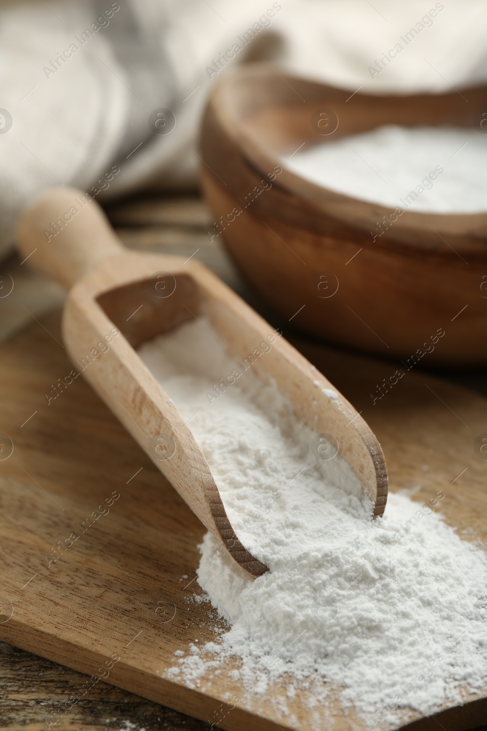 Photo of Baking powder in scoop and bowl on wooden table, closeup