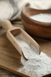 Baking powder in scoop and bowl on wooden table, closeup