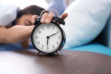 Young woman turning off alarm clock in morning. Bedtime