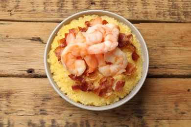 Photo of Fresh tasty shrimps, bacon and grits in bowl on wooden table, top view