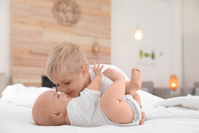 Photo of Cute boy kissing his little sister on bed at home