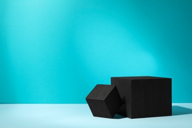 Photo of Black cubes on light table against turquoise background, space for text. Stylish presentation for product
