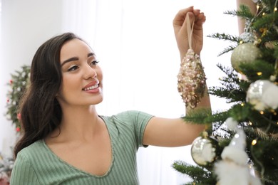 Photo of Young woman decorating Christmas tree at home