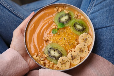 Photo of Woman holding bowl of delicious fruit smoothie with fresh banana, kiwi slices and granola, top view