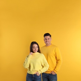 Photo of Happy couple wearing warm sweaters on yellow background