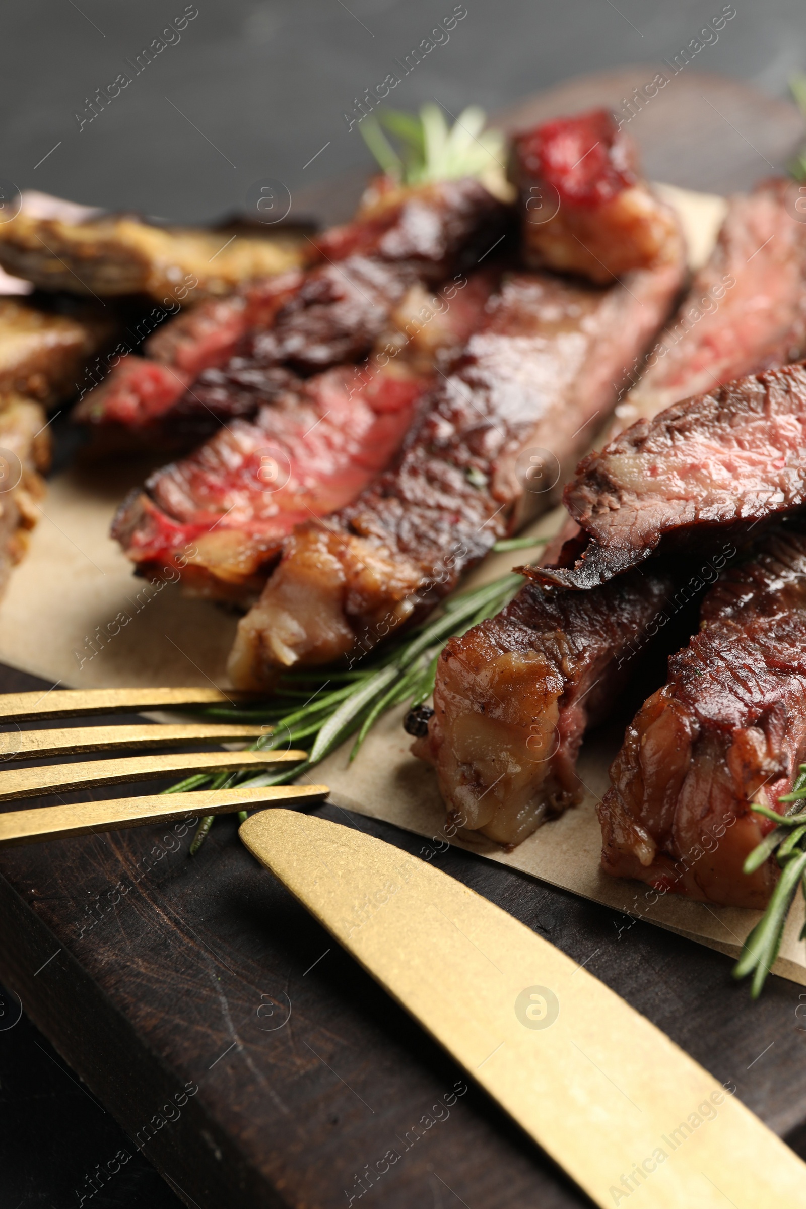Photo of Delicious grilled beef with rosemary served on wooden board, closeup