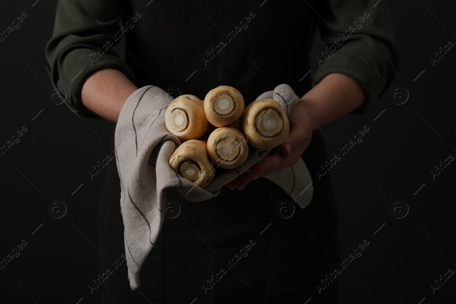 Photo of Woman holding fresh ripe parsnips on black background, closeup