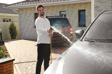 Photo of Young happy man washing car at backyard on sunny day