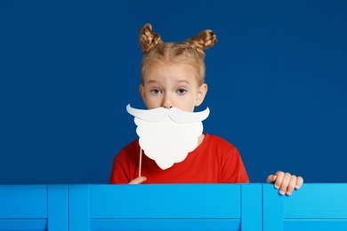 Image of Cute little girl with Santa beard prop on blue background. Christmas celebration