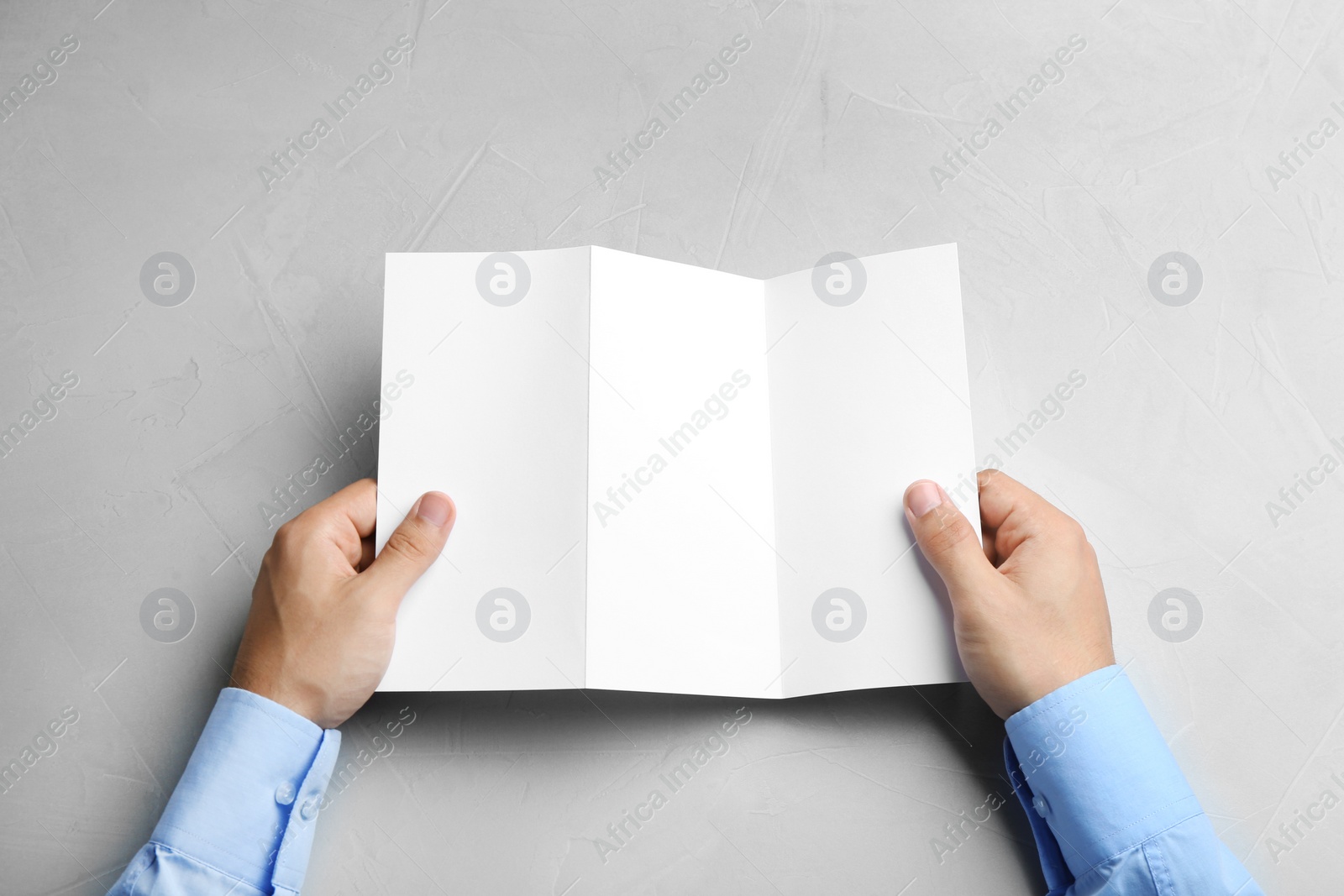Photo of Young man holding blank brochure at grey table, top view. Mock up for design