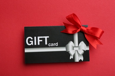 Photo of Gift card with bow on red background, top view