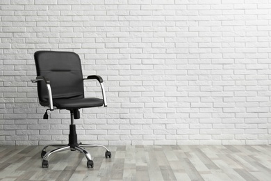 Comfortable office chair near white brick wall indoors. Space for text