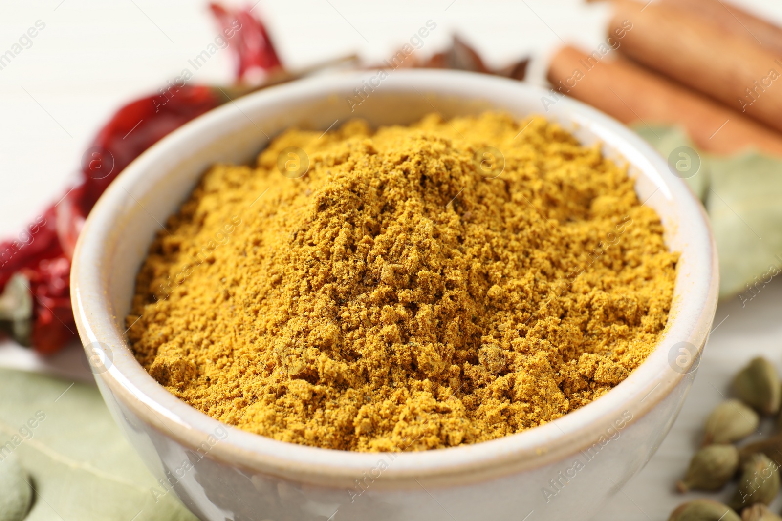 Photo of Curry powder in bowl and other spices on table, closeup