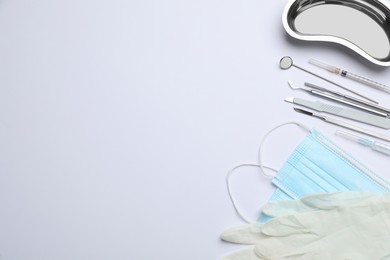 Set of different dentist's tools, face masks and gloves on light background, flat lay. Space for text