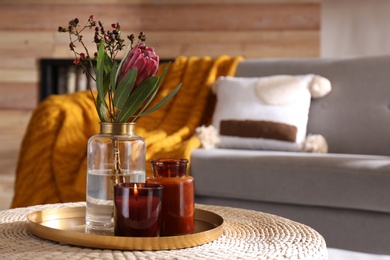 Vase with beautiful protea flower and candles on wicker stand indoors, space for text. Interior elements