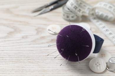 Photo of Blue pincushion with pins and other sewing tools on light wooden table. Space for text