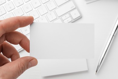 Photo of Woman with blank business card at white table, closeup. Mockup for design
