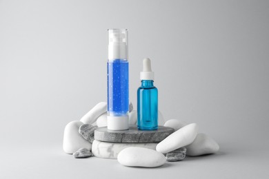 Photo of Bottles of cosmetic products and stones on light grey background