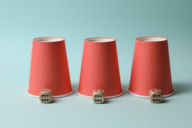 Photo of Three red cups and dices on light blue background. Thimblerig game