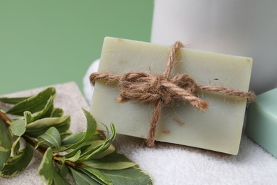 Photo of Soap bar, plant branch and towel on green background, closeup