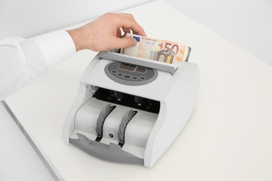 Photo of Man putting money into counting machine on table, closeup