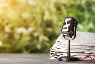 Image of Newspapers and vintage microphone on table against blurred green background, space for design. Journalist's work