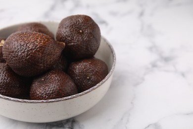 Photo of Fresh salak fruits in bowl on white marble table, closeup. Space for text