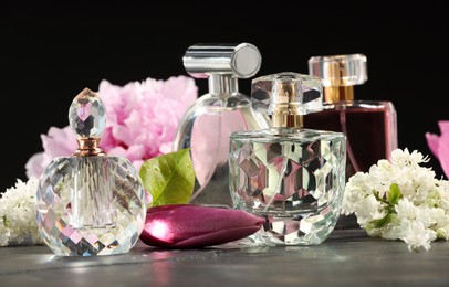 Photo of Luxury perfumes and floral decor on grey table against black background