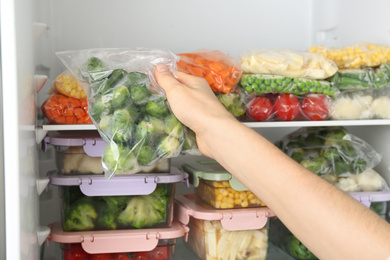 Photo of Woman putting plastic bag with brussels sprouts in refrigerator with frozen vegetables, closeup