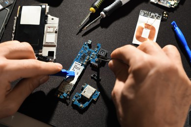 Photo of Technician repairing broken smartphone at table, closeup