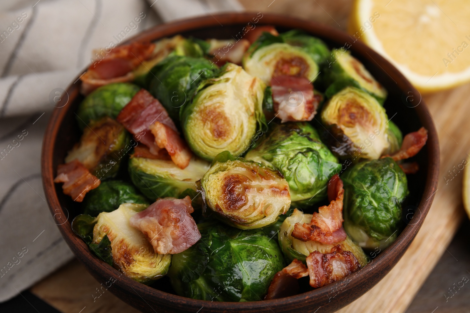 Photo of Delicious roasted Brussels sprouts and bacon in bowl on table, closeup