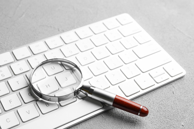 Photo of Magnifier glass and keyboard on light grey stone background, closeup. Find keywords concept