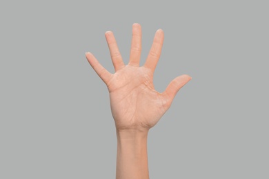 Photo of Woman showing number five on grey background, closeup. Sign language